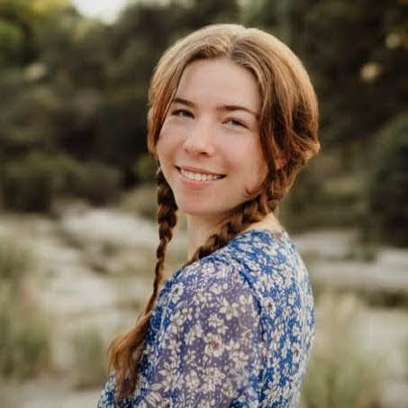Young woman with pigtail braids wearing flowery dress smiles at camera